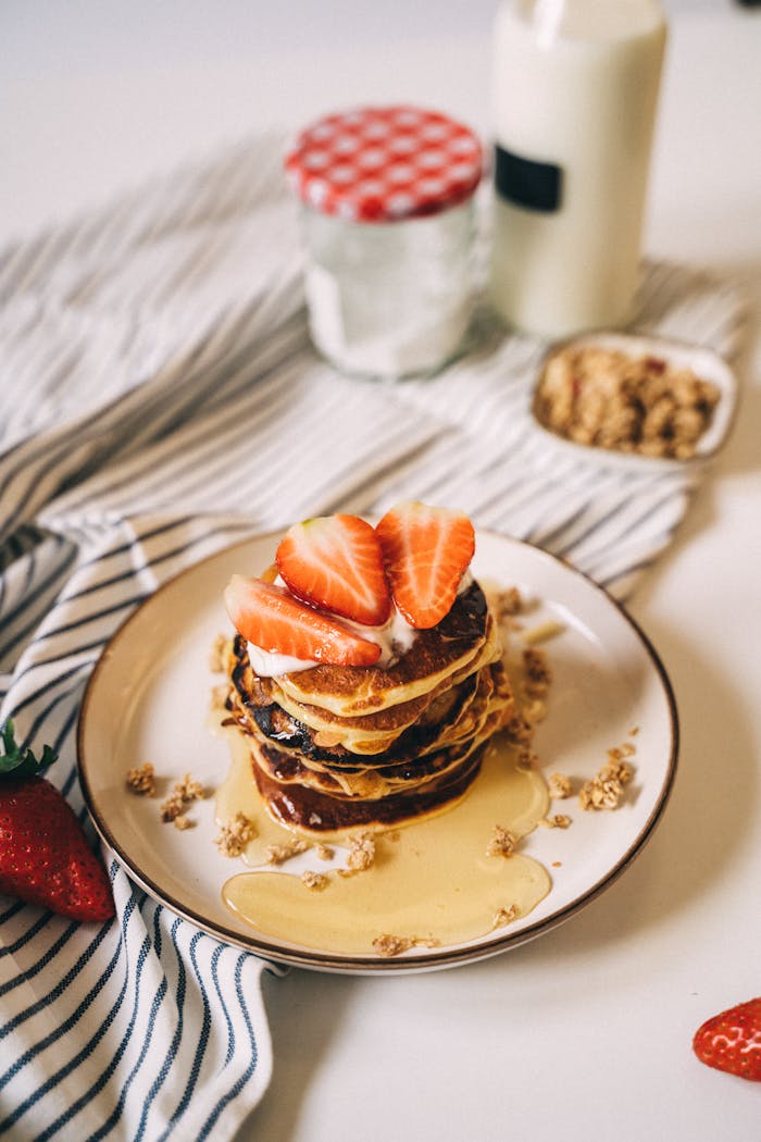 Stack of pancakes topped with strawberries and honey, perfect for breakfast or brunch.