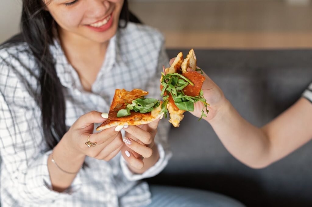 pexels photo 7780235 Two friends share a fun moment enjoying tasty pizza slices indoors. A joyful culinary experience.